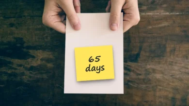 Two hands holding a blank white card over a dark wooden table, with a sticky note reading “65 days”.