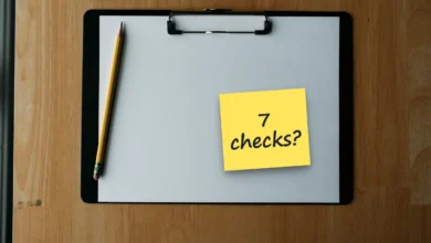 A blank sheet on a black clipboard with a yellow pencil on a wooden desk, with a sticky note reading “7 checks?”.