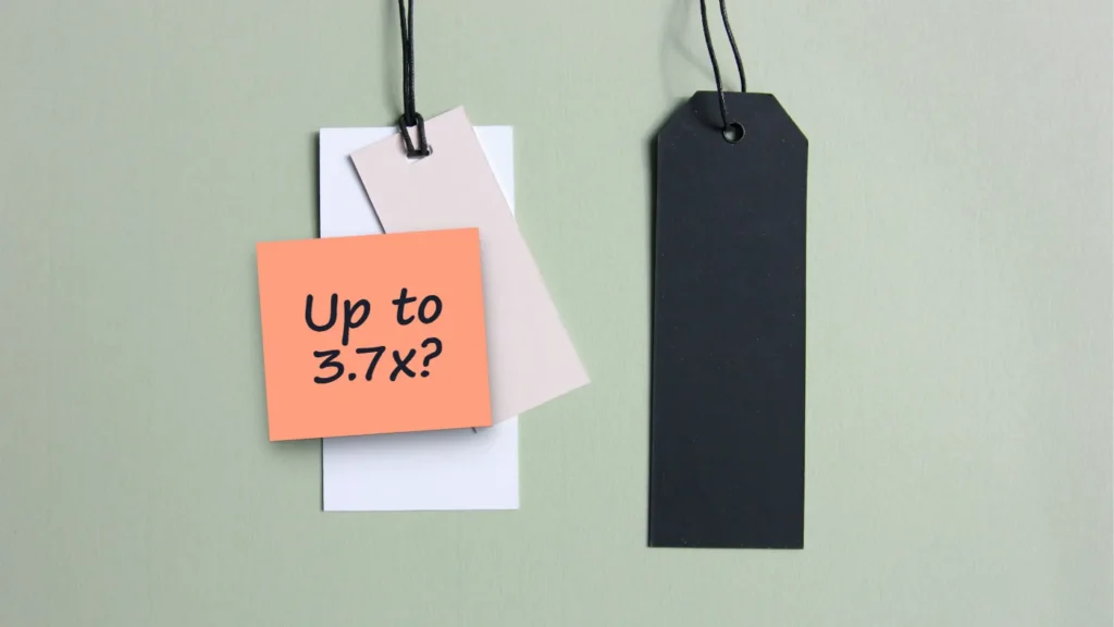 Two blank hang tags, one white and one black, on a sage-green background, with a sticky note reading “Up to 3.7x?”.