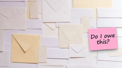 White and cream envelopes laid out on a table, with a sticky note reading “Do I owe this?”.
